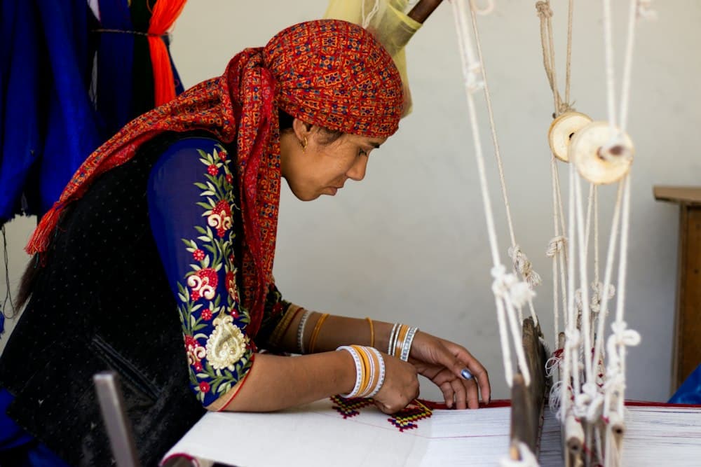 Woman in a red head scarf bent over her worktable doing hand embroidery