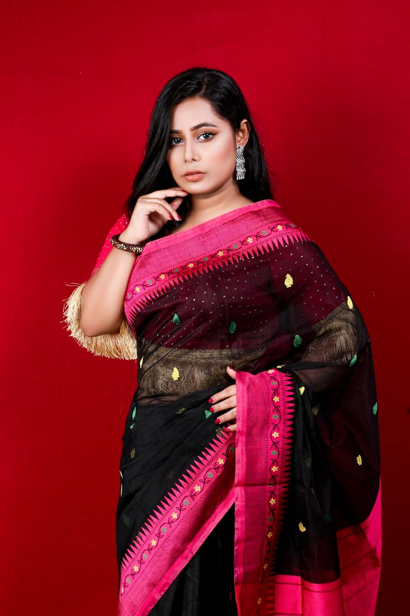 Woman in a black saree with a rani pink border against a red backdrop