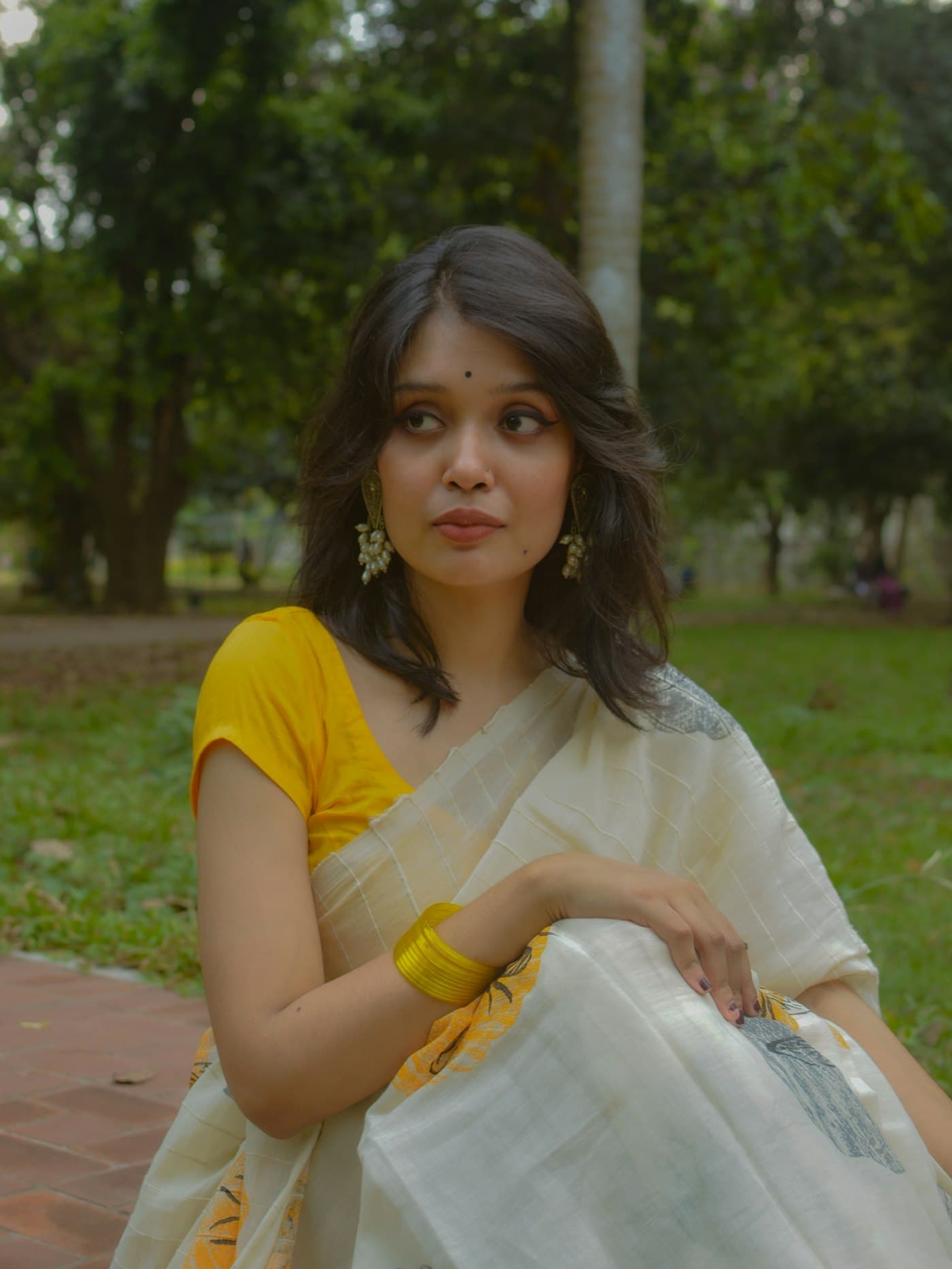 Woman in an ivory and gold kasavu saree with a yellow blouse, seated in a garden