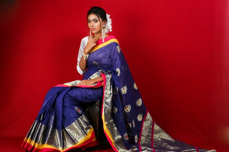 Woman seated in a navy and gold Kanjivaram silk saree against a red backdrop