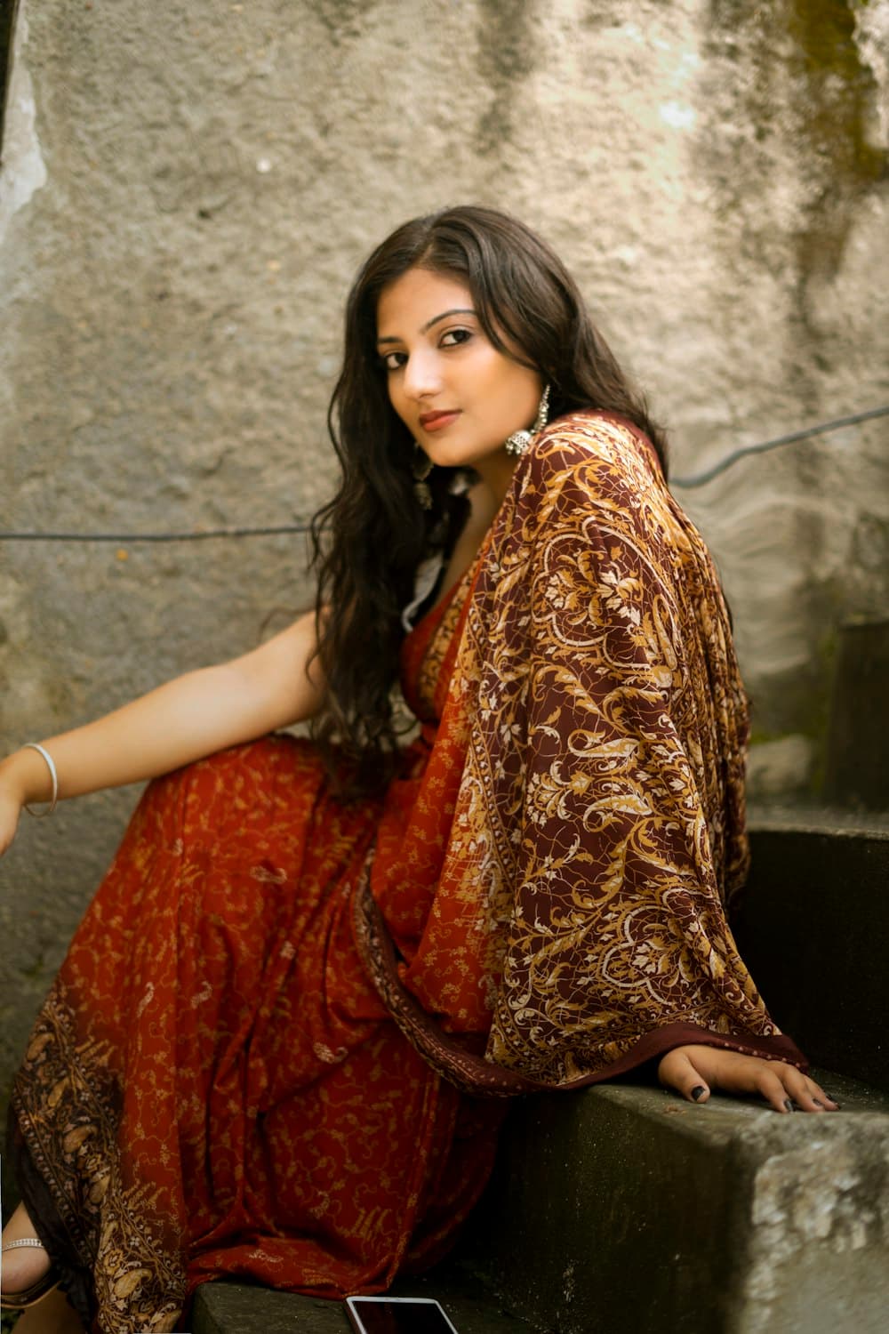 Woman in a rust and brown printed saree seated on concrete steps