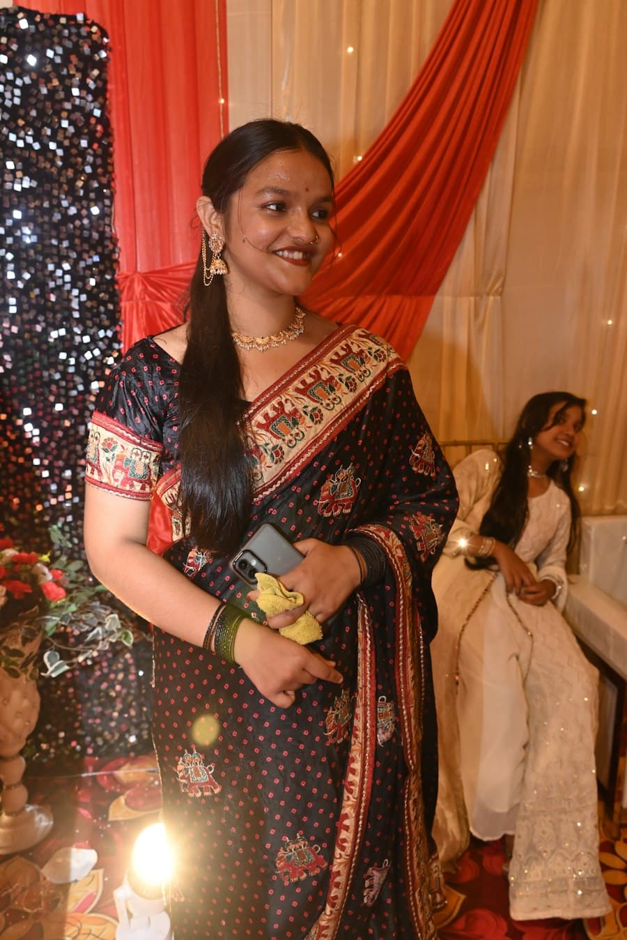 Woman in a black and gold saree standing in front of a red curtain
