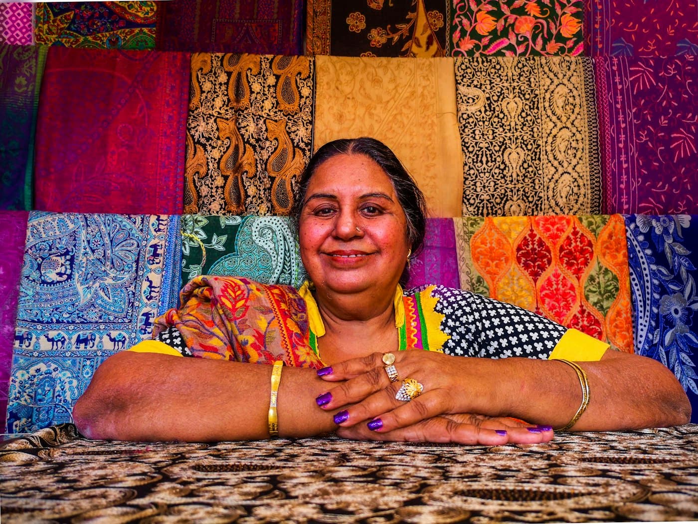 Smiling woman resting her arms on a counter in front of stacked block-printed textiles
